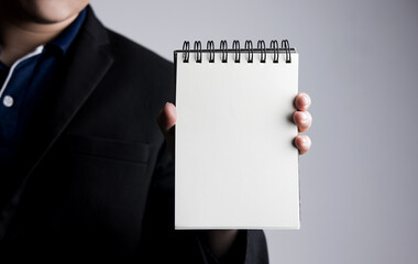 Man in suit standing holding blank white notebook page on gray background. with copy space, insert...