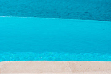 Fototapeta na wymiar Summer vacation at poolside. Infinity swimming pool with sea on bright summer day
