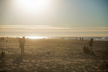 Crowds of people enjoying a day out at the beach in winter sunshine - obrazy, fototapety, plakaty