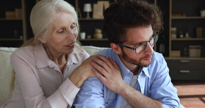 Close up older woman comforting upset adult son, talking sit on sofa. Mature granny give wise advice in difficult life situation to grow up grandson, help get through divorce break up. Support concept