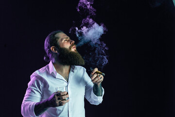 hipster bearded man in white shirt blowing smoke holds glass of whiskey and cigar. Studio shot
