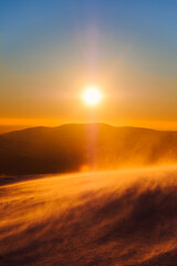 Russia. Sheregesh. A beautiful sunset in orange and blue tones among mountains and snow. Snowstorm. Snow glitters in the sun