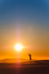 The silhouette of a snowboarder who holds a snowboard in his hands, against the sunset in orange...