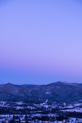 Russia. Sheregesh. Sunset in purple tones. View of snowy mountains and forest