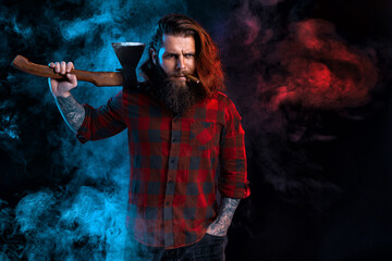 Fototapeta na wymiar Bearded lumberjack. Brutal man with cigar in checkered shirt with long hair holds old axe in smoke