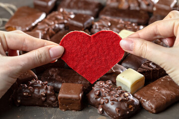 Appetizing food background. Assortment of chocolate handmade candy and red heart card for valentine's day in female hands. Chocolate background. 
