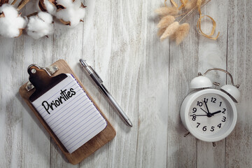 PRIORITIES text on notepad rustic wood flat lay with alarm clock and natural elements.  Time management concept.