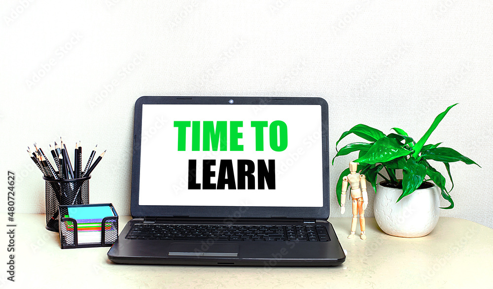 Poster on the desktop is a potted plant, stationery and an open laptop with the text time to learn on the s