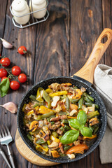 Seafood ragout, healthy mediterranean dinner. Seafood shrimps, calamari, cuttlefish stewed with vegetables and garlic sauce in a frying pan, on an wooden table. Copy space.