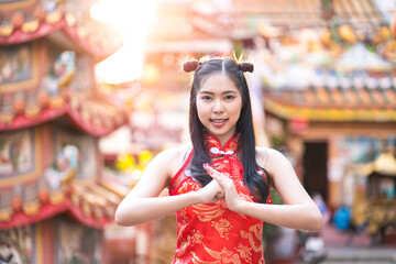 Fototapeta premium Portrait beautiful Asian girl wearing red traditional Chinese cheongsam decoration with gesture of congratulation at Chinese shrine for Chinese New Year Festival