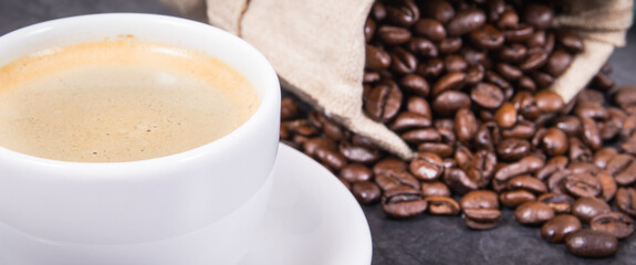 White cup of coffee and roasted fragrant dark coffee grains in bag