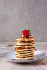 a thin trickle of honey pours on strawberries on a stack of pancakes