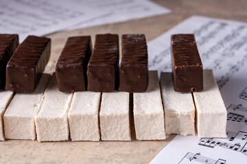 Piano keyboard made of white and chocolate marshmallow lies on music paper, selective focus