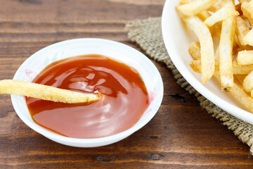 Potato sticks close up in white dish and chilli sauce on an wooden table, snack food