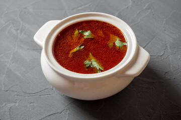 Close-up of soup borscht in a white ceramic soup bowl on a gray textured background. Traditional soup for Russia and Ukraine. Greens float on top of the soup. Side view