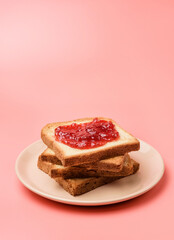 A stack of toasts with jam on a dish close-up. Plate with pieces of toasted bread on a pink background with copy space.