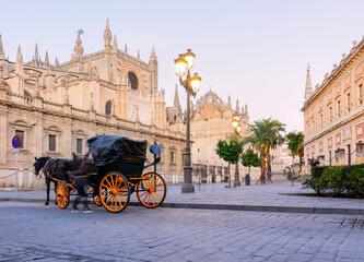 Fototapeta na wymiar Seville, Spain, Facade of the Cathedral of Gothic in Seville, Spain. Wagons with horses for riding tourists in the background of the cathedral - sunset