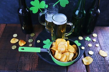 Patrick Day, foamy beer in glass mugs and a bottle, paprika chips, gold coins, on a red wooden table, a green shamrock on a dark background, a party, a congratulation, a postcard - Powered by Adobe