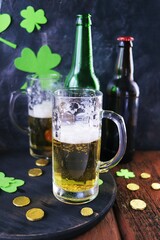 Patrick day, foamy beer in glass mugs and a bottle, gold coins on a wooden table, green shamrock on a dark background, party, congratulation, postcard