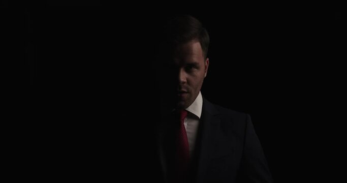 mysterious young man in suit moving in a back view position and walking away in the dark on black background in studio