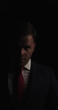 project video of sexy young businessman in the dark fixing tie, rubbing fingers through hair and adjusting hairstyle on black background in studio