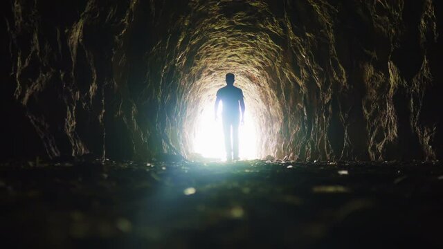 A man goes through a dark tunnel to a bright light, the concept of the exit of the soul to God's light, the mystical movement of the silhouette of a man