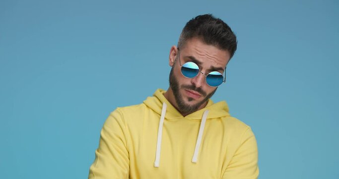handsome casual man wearing sunglasses, trying to observe something better then smiling and pointing at the camera