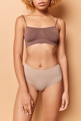 Obraz premium Wellness women body and slimming concept. Cropped shot of unrcognizable woman dressed in top and panties has flat belly healthy smooth skin and slender legs isolated over beige studio background