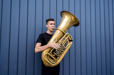 Young street musician playing the tuba near the big blue wall