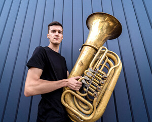 Young street musician playing the tuba near the big blue wall