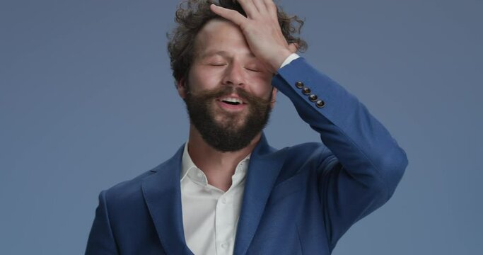 happy bearded man with moustache face palming, smiling, nodding and making a warning finger gesture on blue background in studio