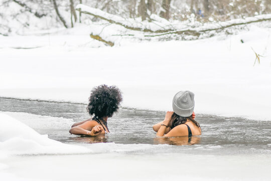 Couple of beautiful girls enjoying winter and swimming in the cold water of a lake or river, cold therapy, ice swim with white winter landscape