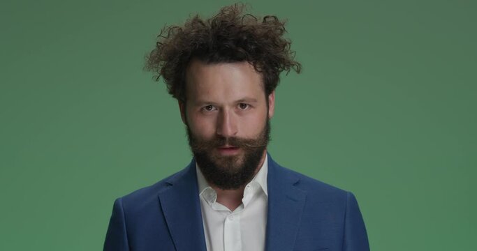 dynamic, energy young man in elegant suit having fun in front of green background, shaking head and laughing in studio