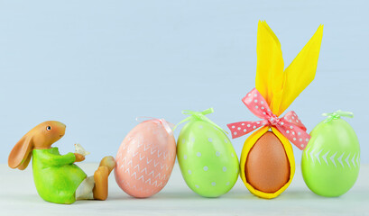 Easter rabbit next to painted multicolored Easter eggs on a wooden background. Copy Space.