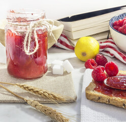 glass jar with raspberry jam next to wheat bread toast with raspberry jam. background decoration...