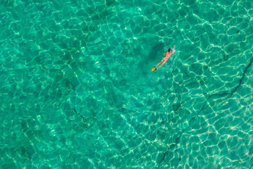 Alone naked nudist man dives in flippers, snorkeling mask and tube swimming in sea, ocean turquoise clear water. Top view. Aerial, drone, copter view.