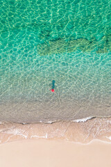 Top view. Young beautiful woman in red hat standing and sunbathe in sea water. Drone, copter photo. Summer vacation. View from above.