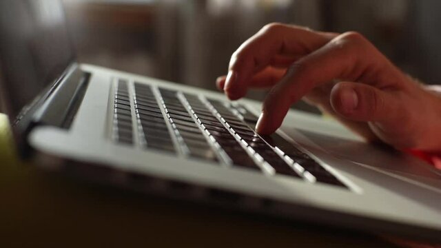 Extreme close-up hands of unrecognizable business man typing on keyboard of laptop computer at dark room. Freelancer using notebook working overtime from home at night. Shooting in slow motion.
