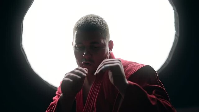 Taekwondo practitioner in a red kimono is boxing in front of him in a gym. Slow motion