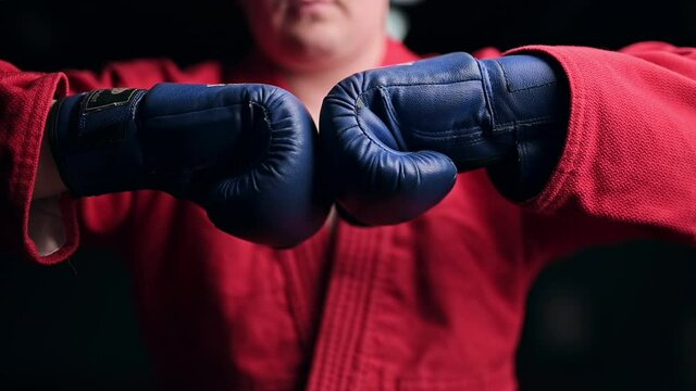 Taekwondo practitioner in a red kimono and gloves is boxing in front of him in a gym. Slow motion