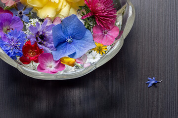 Fototapeta na wymiar Runde Glasschale mit schönen Blumen steht auf dunklem Holz mit Struktur