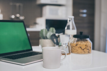 Table set for breakfast, kitchen in the background. Natural meal and technology devices. Interior view of a cozy and modern home. Millennial, youth, home working, home schooling, remote work concept.