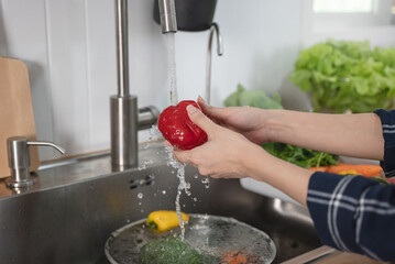 Close up of hands people washing vegetables by tap water at the sink in the kitchen to clean ingredient prepare a fresh salad.