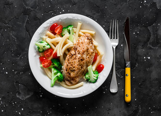Casarecce pasta with broccoli, cherry tomatoes and baked chicken breast on a dark background, top view