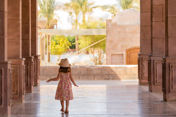 Pretty little girl walks slowly down the portico among the columns. Rear view. El Mustafa Mosque,...