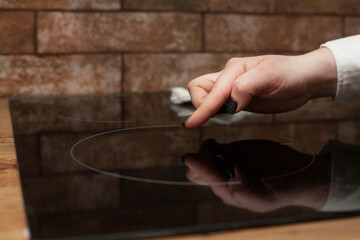 A young woman is cleaning an induction electric hob. Cleaning in the kitchen. Electric oven...