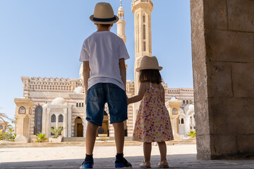 A boy and a girl standing in front of El Mustafa Mosque holding hands and looking at it. View from...