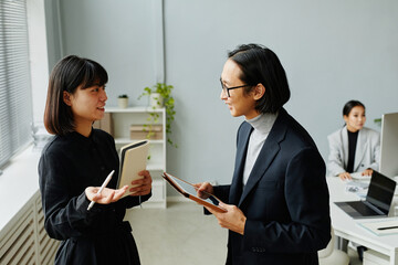 Side view waist up portrait of young Asian businesswoman talking to manager while standing in office