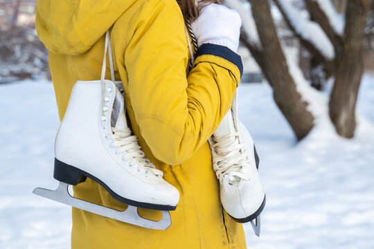 Close up of female hands holding ice skates. Young woman in yellow coat with skates. Back view.