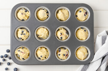 Raw dough for lemon muffins with blueberries and shtreisel in baking form on a white wooden background. Recipe step by step. Top view.